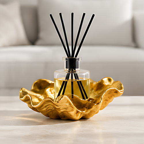 Reed diffuser with black sticks and a clear bottle of golden liquid in a sculptural gold-toned base